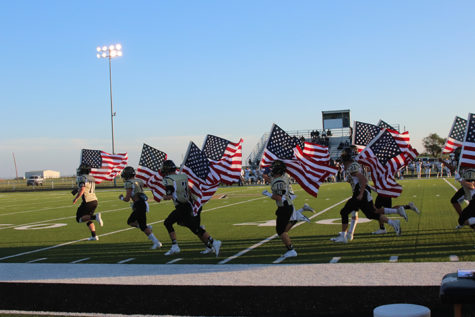 The Wildcat varsity football team runs on to the field carrying American flags. 