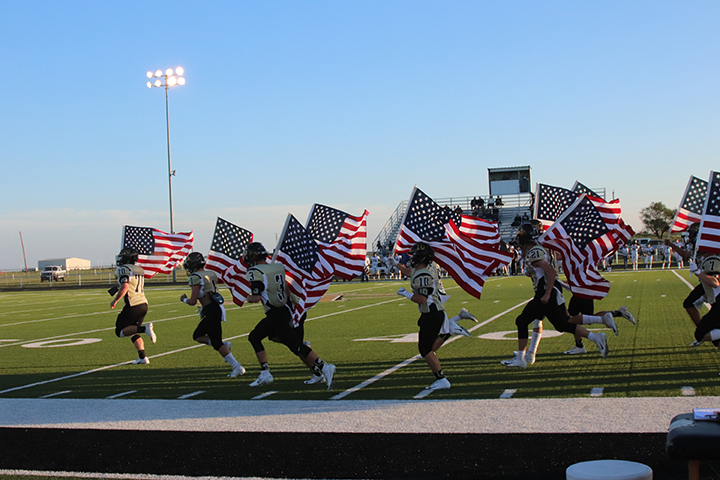 The+Wildcat+varsity+football+team+runs+on+to+the+field+carrying+American+flags.+