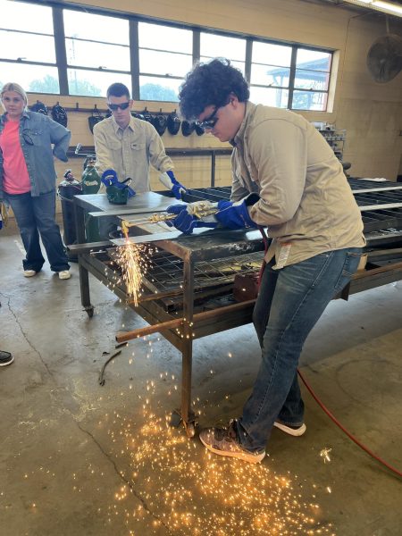 While junior Sam Gilmore waits, senior Johnathan Clay practices using the welding torch.  